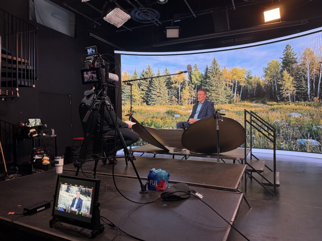 Behind-the-scenes view of a television studio filming an interview with a nature backdrop screen
