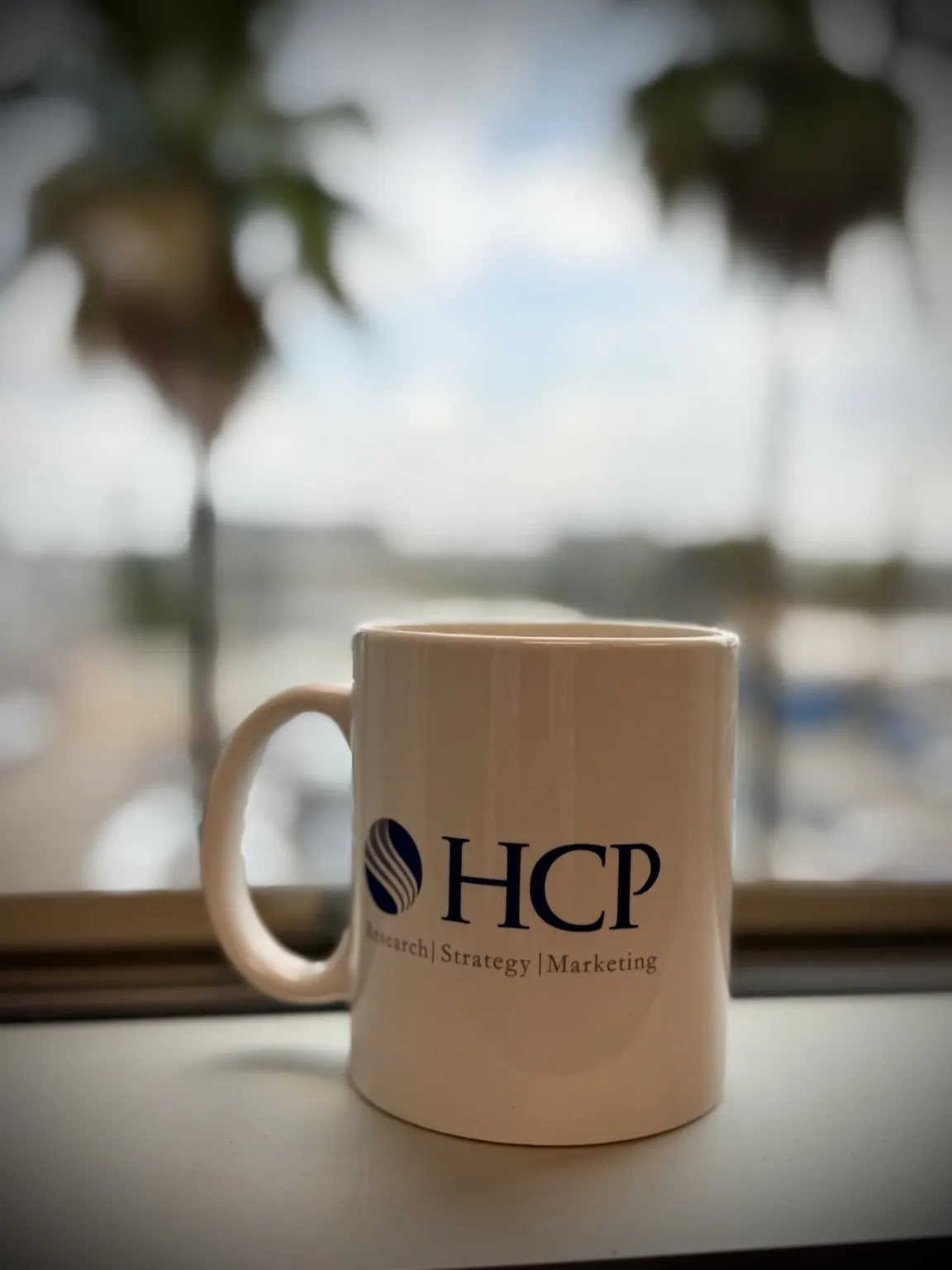 HCP Associates branded coffee mug on a windowsill