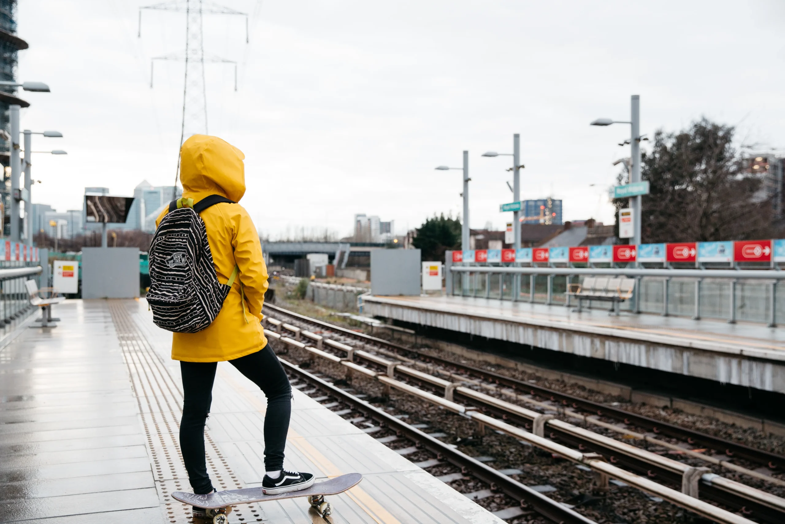 Person skateboarding along train tracks, wearing a yellow jacket and backpack