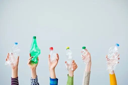 Hands holding up different colored plastic bottles for recycling