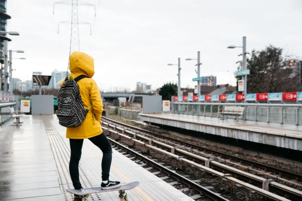 Person skateboarding along train tracks, wearing a yellow jacket and backpack
