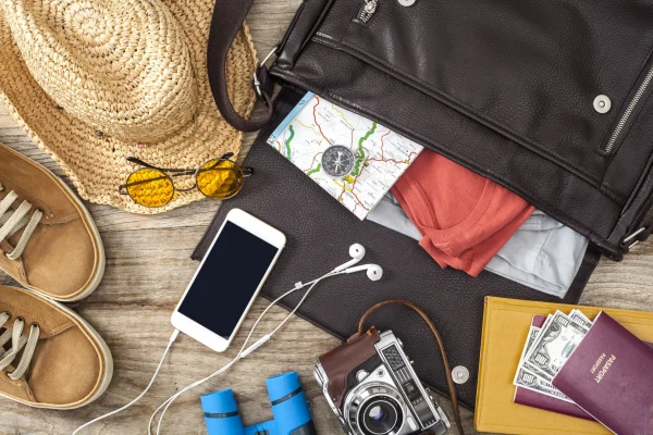 Flat lay of travel essentials including a hat, shoes, phone, and passport